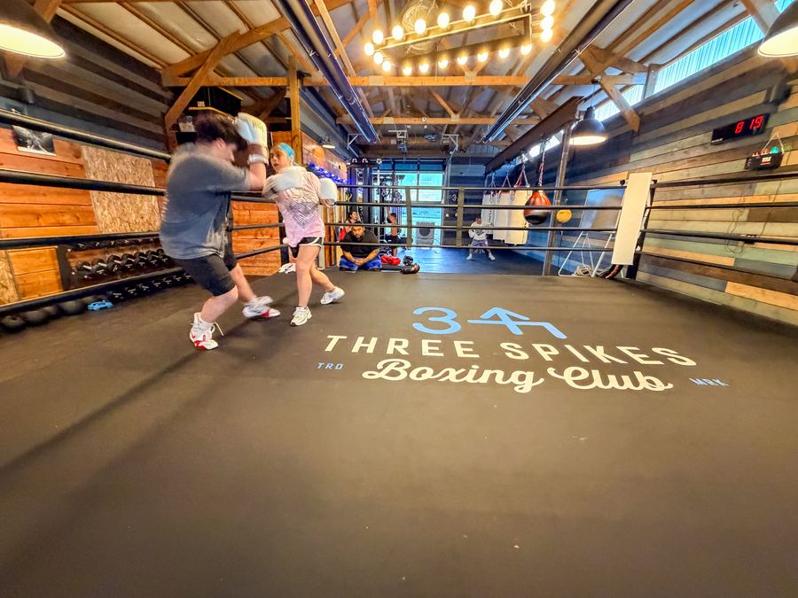 Two boxers sparring across the Three Spikes logo on the ring floor