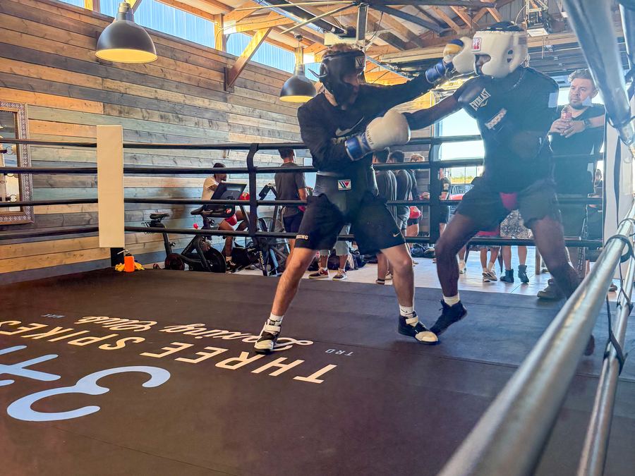 Two boxers in headgear sparring while the club watches from ringside